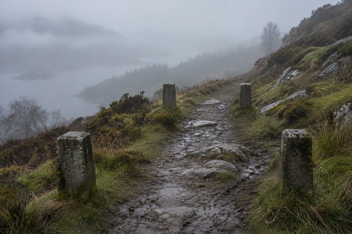 Quattro paletti di cemento lungo un sentiero fangoso nella nebbia